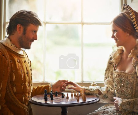 Renaissance, couple et échecs à la maison avec la main, costume vintage et médiéval dans un palais. Fenêtre, luxe et reine avec sourire du jeu de stratégie et de parler tout en jouant avec l'amour.