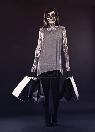 Photo for Woman, skull makeup and shopping bags in studio on dark background with retail and discount for halloween. Portrait, female person and tattoo with edgy or creative style, body art and confidence. - Royalty Free Image