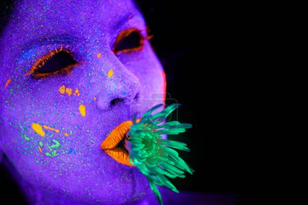Téléchargez les photos : Néon, peinture et visage de femme avec de l'art en studio ou plante pour la créativité organique, esthétique psychédélique ou espace de maquette. Maquillage lumineux, personne ou paillettes fluorescentes pour illusion UV sur fond noir. - en image libre de droit