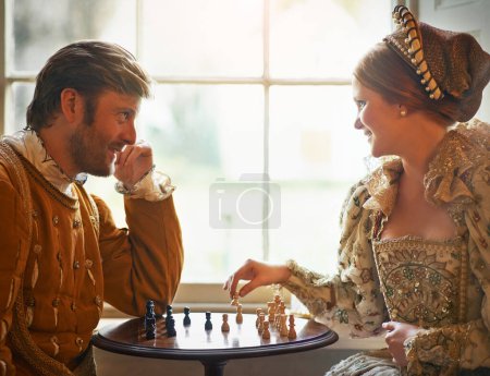 Renaissance, couple et échecs à la maison avec sourire, costume vintage et médiéval dans un palais. Fenêtre, luxe et reine avec sourire du jeu de stratégie et de parler tout en jouant avec l'amour.