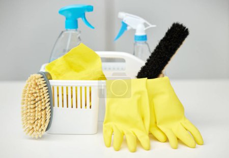 Photo for Table, brush or basket with cleaning supplies, spray bottle or chemical for bacteria, wellness or dirty mess. Grey background, maid service or ready for washing with product, liquid soap or gloves. - Royalty Free Image