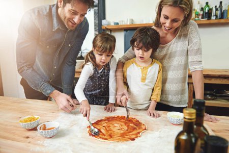 Photo for Parents, kids and happy for cooking pizza with sauce, learning and helping hand for development in kitchen. Mother, father and children with dough, teaching and support with bonding in family house. - Royalty Free Image