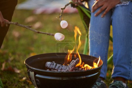 People, toasting and marshmallow by fire on camping in forest with love or bonding for adventure. Man, woman and smores with grill for dessert by flame in nature on vacation for memories on picnic.