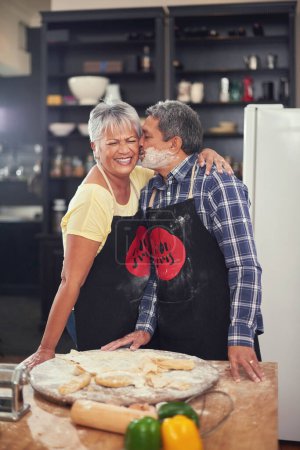 Photo for Cooking, kiss and senior couple in kitchen at home with dough, flour and ingredients for meal. Happy, food and elderly man and woman preparing dinner, lunch or supper together at house in Mexico - Royalty Free Image