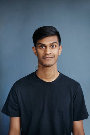 Studio, portrait and smile of Indian student, confidence and guy with tshirt, fashion and college. University, gen z and male person, school and blue background, pride and face of model and yearbook.