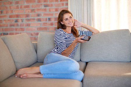 Photo for Woman, remote control and smile on sofa for television, relax and calm in living room. Young person, happy and watching tv show or streaming movie and documentary on couch with joy for weekend. - Royalty Free Image