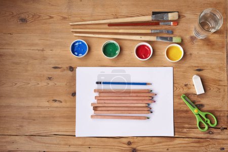 Photo for Desk, paint and brush with stationery for school project or assignment on creative art, design and drawing. Wooden table, supplies and pencil for writing exams or test with blank page for ideas - Royalty Free Image