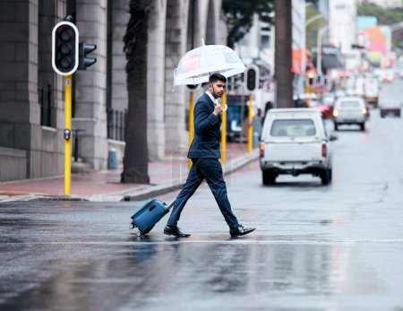 Photo for Businessman, walking and city with umbrella on street for travel, work or business trip in winter. Man, employee or pedestrian crossing road with luggage for commute or immigration in an urban town. - Royalty Free Image