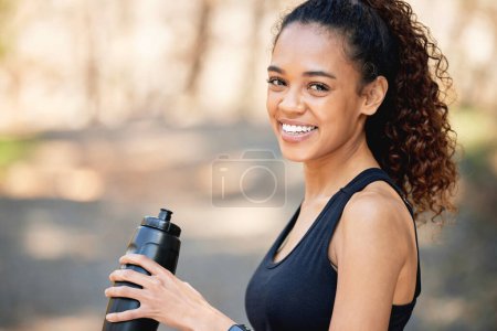 Mujer, retrato y agua potable en botella o bosque caminando para ejercitar la salud, hidratación o electrolitos. Persona femenina, rostro y sonrisa en el sendero de montaña para entrenamiento matutino, fitness o running.