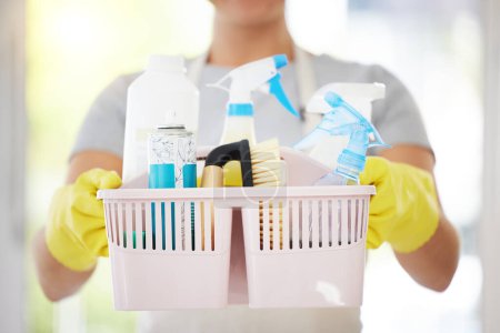 Person, hands and basket with cleaning supplies for disinfection, housekeeping or domestic detergence. Closeup of cleaner or maid with bucket, gloves or chemicals for bacteria or germ removal service.