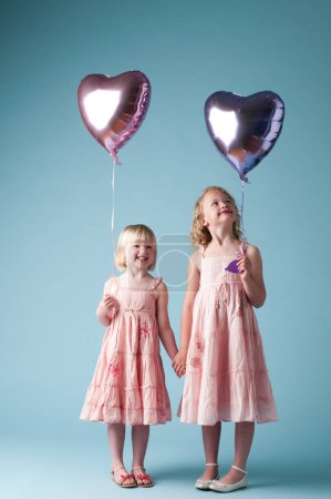 Photo for Children, holding hands and sister with heart balloon in studio on blue background for family or party. Birthday, celebration event or happy with smile of girl kids on color backdrop together. - Royalty Free Image