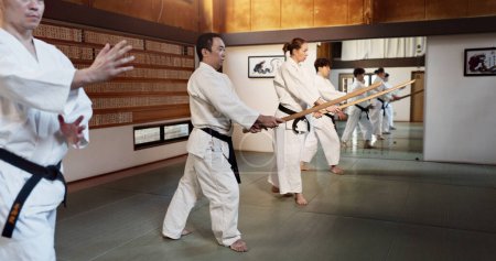 Téléchargez les photos : Aïkido, bâton et classe de combat avec entraînement à l'arme et épée en bois pour l'exercice d'autodéfense. Dojo, les étudiants et les personnes dans une salle de gym ou un studio avec entraînement, pratique de la ceinture noire et de remise en forme au Japon. - en image libre de droit