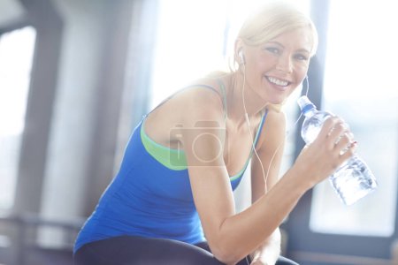 Photo for Earphones, water and portrait of woman in gym listen to podcast, music or radio with hydration. Health, exercise and female athlete streaming song, album or playlist for workout in fitness center - Royalty Free Image
