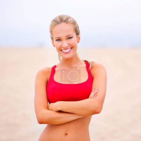 Femme, portrait et exercice sur la plage avec bras croisés, confiance et sourire avec bien-être et extérieur. Fitness, athlète et sport avec bonheur pour la santé, marathon ou course pour l'entraînement cardio.