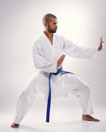 Studio, Karate und schwarzer Mann mit Kampfkunst, Training und blauem Gürtel für Instruktor vor weißem Hintergrund. Disziplin, männliche Person und Erwachsener mit Technik für Gesundheit, goju ryu und Bewegung für Macht.
