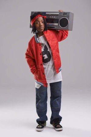 Foto de Niño africano, hip hop y retrato de moda con radio para música rap y danza en un estudio con ropa urbana. Niño negro y boombox con ropa de moda y botín con confianza y fondo gris. - Imagen libre de derechos
