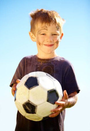 Photo for Portrait, smile and child with soccer ball outdoor for sports, exercise or game in summer. Face, boy and happy kid with football with mud, messy or dirty for recreation in Switzerland on blue sky. - Royalty Free Image