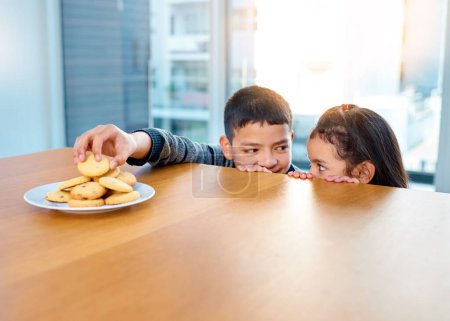 Photo for Home, brother and sister in kitchen, biscuits and siblings together, boy and girl in morning or hungry. House, kid and cute child for food or cookies on table, plate and bonding or dessert in weekend. - Royalty Free Image