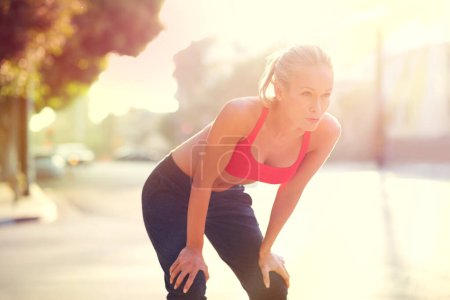 Photo for Tired woman, rest and fitness with break in city after workout, running or cardio exercise. Exhausted or determined female person or athlete in recovery, training or breathing from run in urban town. - Royalty Free Image