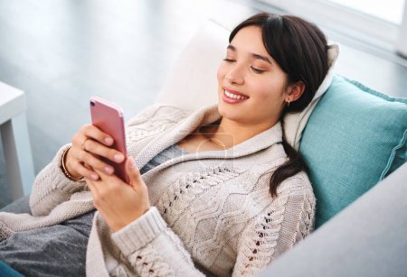 Asian woman, home and smile on couch with smartphone, text and messages with dating app and social media. Above, female person and online for post, content update and happy with internet videos