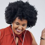 Laughing, dance or happy black woman in music headphones in studio for singing on grey background. Model, funny podcast or African person listening to radio playlist, sound or comedy audio with smile.