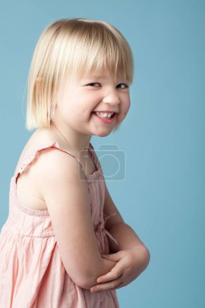 Photo for Little girl, smile and playful in studio with portrait for child development on blue background. Sneaky, rascal and confident in childhood with youth for joy with fun, happy and innocent cute face. - Royalty Free Image