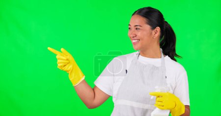 Foto de Mujer asiática feliz, ama de llaves y apuntando a pantalla verde con detergente para una higiene limpia. Retrato de mujer, mucama o limpiadora para publicidad con botella de spray sobre fondo de estudio. - Imagen libre de derechos