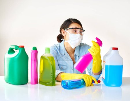 Photo for Detergent bottles, gloves and woman with mask or glasses for protection, safety and cleaning at home. Housekeeping, cleaner or female person with products, liquid container or spray on table for dust. - Royalty Free Image