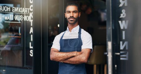 Proud waiter, man and arms crossed at restaurant for business, welcome or ready for service with confidence. Barista, person and server by entrance of cafe, coffee shop or diner for hospitality and c.