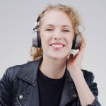 Portrait, music or happy woman in headphones in studio for singing or wellness on grey background. Model, face or girl listening to radio playlist, sound or podcast audio with smile or subscription.