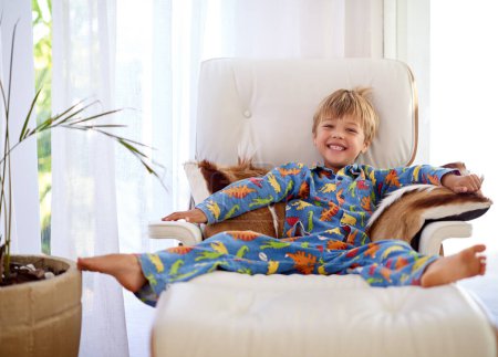 Foto de Niño, retrato y feliz en el sofá, sofá o sillón reclinable en casa para el fin de semana, vacaciones o vacaciones escolares. Niño, sonrisa y pijama juguetón en la sala de estar para vacaciones, relajarse y disfrutar de la mañana. - Imagen libre de derechos