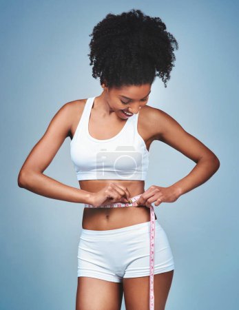 Téléchargez les photos : Girl, happy and tape on stomach in studio to measure weight loss, progress of diet and daily exercise. Woman, grey background and measurement for improvement of new prescription drug or tummy tuck - en image libre de droit