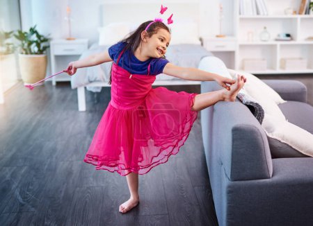 Foto de Niña, danza y traje de hadas en casa para el ballet, el desarrollo y la actividad creativa. Jovencita, estirando y jugando en vestido por sofá para princesa, halloween y fantasía divertida como niño. - Imagen libre de derechos
