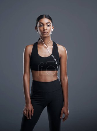 Photo for Indian woman, portrait and headphones in studio for music, listening and fitness by dark background. Gen z athlete, streaming and audio for workout, sports and training with podcast or playlist. - Royalty Free Image