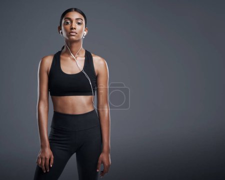 Photo for Indian woman, portrait and headphones in studio for music, listening and fitness by dark background. Gen z female, streaming and audio for workout, sports and training with athlete on mockup space. - Royalty Free Image