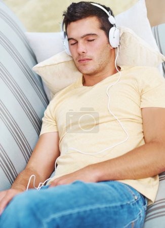 Téléchargez les photos : Homme, sommeil et musique sur canapé, écouteurs et repos dans le salon, se détendre et flux en direct. Épuisé, calme et canapé à la maison pour s'endormir, calme et fatigué ou écouter podcast pour zen. - en image libre de droit