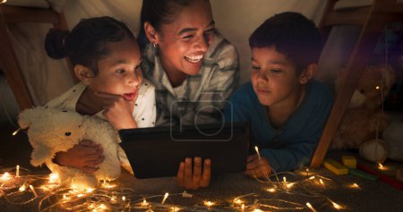 Lustig, Tablet und Mutter mit Kindern in einem Zelthaus, das nachts Internet-Videos, Shows oder Filme online streamt. Dunkel, digital und Eltern oder Vater entspannen mit Kindern, die abends Comedy gucken.