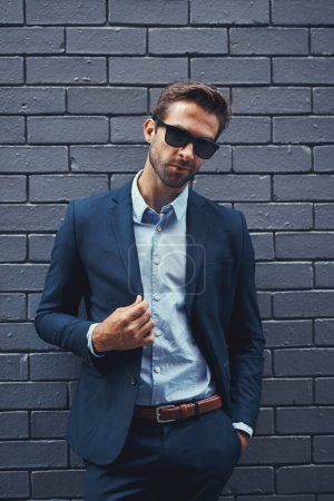 Photo for Male model, wall and fashion with suit or confident for clothing, sunglasses or trendy and cool. Businessman, backdrop and stylish or formal for career with corporate, lawyer with hands in Chicago. - Royalty Free Image