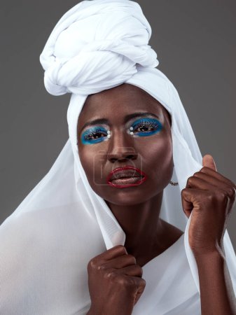 Portrait, Afrikanerin und Frau in traditioneller Kleidung oder Mode mit Make-up, Kosmetik und Kopftuch im Studio. Weibliche Person, stilvoll und selbstbewusst für Erbe, Stolz und Kultur vor grauem Hintergrund.