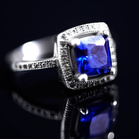 Photo for Sapphire, silver ring and studio by black background for closeup, vintage product and luxury. Tanzanite, blue gemstone and white gold with precious metal for jewelry, shine and glow with reflection. - Royalty Free Image