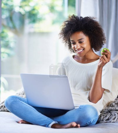 Photo for Apple, fresh produce and woman on sofa with laptop for social media, lifestyle blog and food website at home. Happy female person, technology and fruit for nutrition, healthy diet and clean eating. - Royalty Free Image