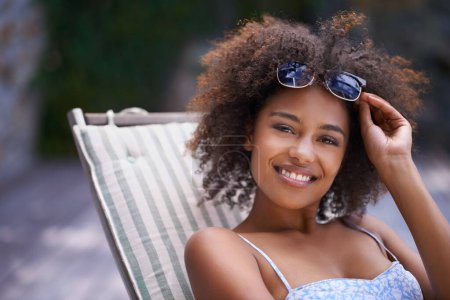 Photo for African, woman and sunbathing and relax, holiday for summer on vacation and sunglasses for time fun. Happy, smile or female person laying on resort deck, comfortable or wellness patio furniture. - Royalty Free Image