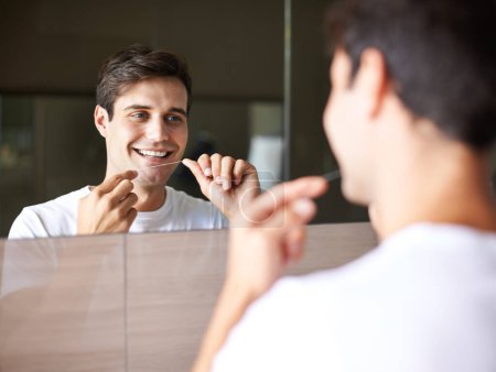 Photo for Happy man, teeth and dental care with floss for hygiene, grooming or freshness in bathroom mirror at home. Face of handsome male person with smile in routine for oral, mouth or gum cleaning at house. - Royalty Free Image