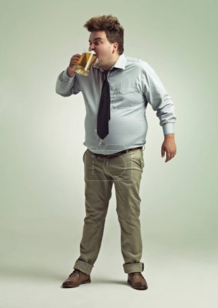 Photo for Man, face and drinking with beer for party or chug in obesity on a studio background. Young male person or plus size model with glass, mug or alcohol in satisfaction for brew or booze on mockup space. - Royalty Free Image