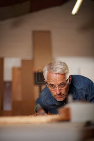 Photo for Carpenter, mature man and working with wood in workplace of workshop as construction worker in company. Employee, male person and professional thinking with glasses for safety in garage and shop. - Royalty Free Image