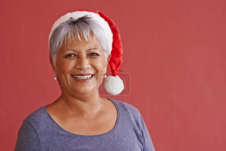 Photo for Portrait, smile and Christmas hat with senior woman, retirement and happiness on red studio background. Face, old person and elderly lady with joy or Xmas with celebration, cheerful or festive season. - Royalty Free Image