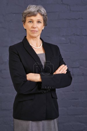Photo for Mature woman, arms crossed and corporate professional with serious face, pride and ambition on wall background. Management, confidence in portrait and real estate agent in London with business. - Royalty Free Image