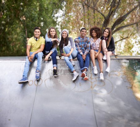 Foto de Retrato, feliz y grupo de adolescentes en skatepark en la ciudad para la unión, divertirse y sentarse juntos. Sonrisa, diversidad y jóvenes amigos z z con el patín en la ciudad para la práctica o la formación - Imagen libre de derechos