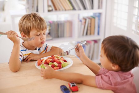 Kinder, Jungen und essen Obstsalat zum Mittagessen im Speisesaal für Ernährung, gesunde Mahlzeit und Wellness zu Hause. Geschwister, Kinder und Frühstücksschale mit Wassermelone, Trauben und Beeren zum Teilen.