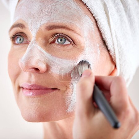 Photo for Mature woman, face mask and brush with happiness in studio for skincare or anti aging on self care, wellness and fresh skin. Closeup, female person and glow with smile for facial and beauty or luxury. - Royalty Free Image